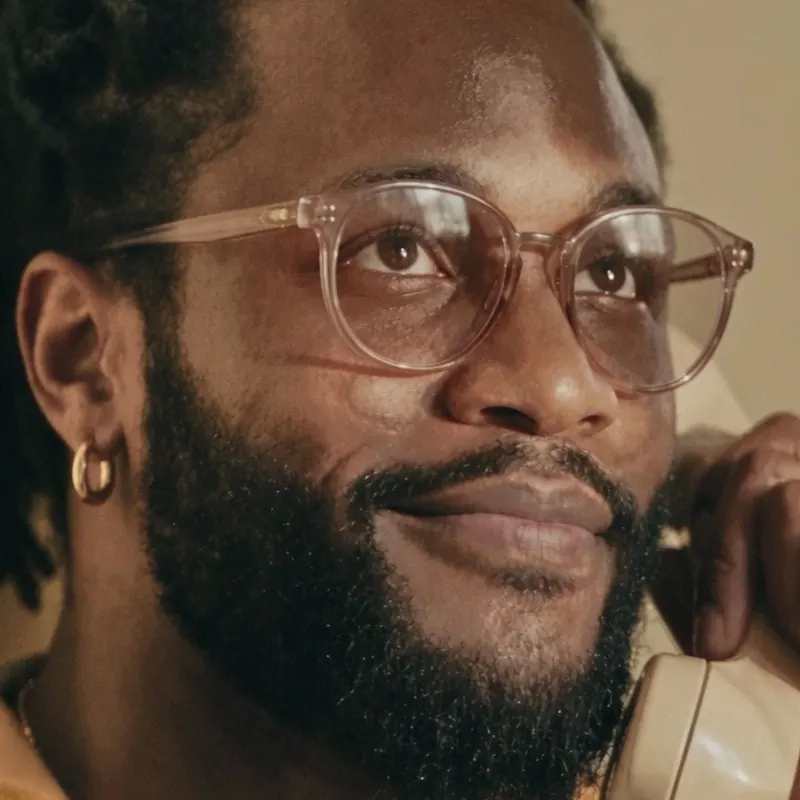 Mike on a cream rotary phone, pink round glasses, gold hoop.
